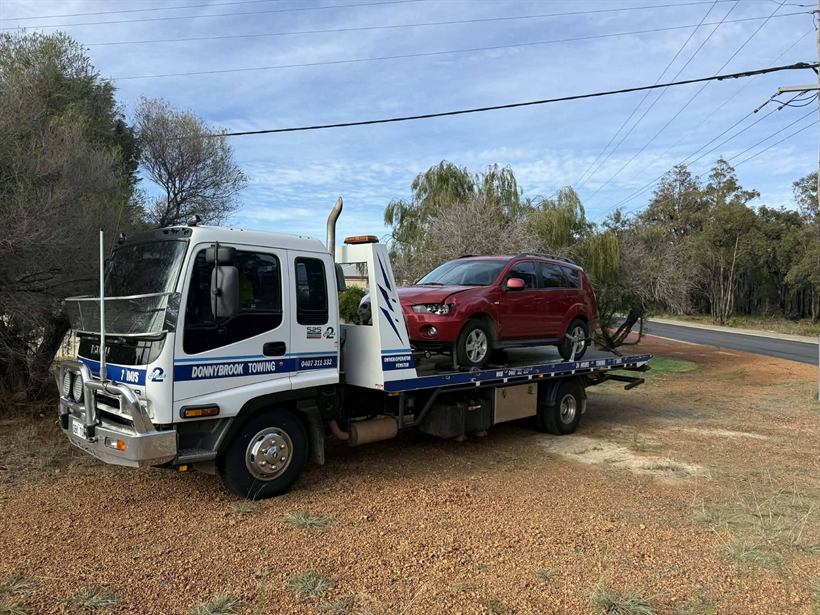 Red car loaded on the tilt tray beside a country road