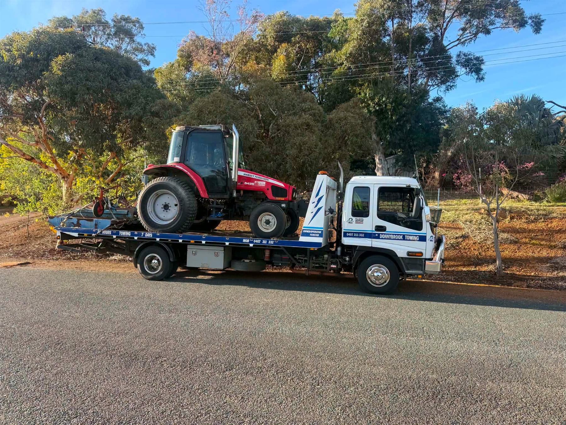 Red tractor strapped down on the Donnybrook Towing tilt tray